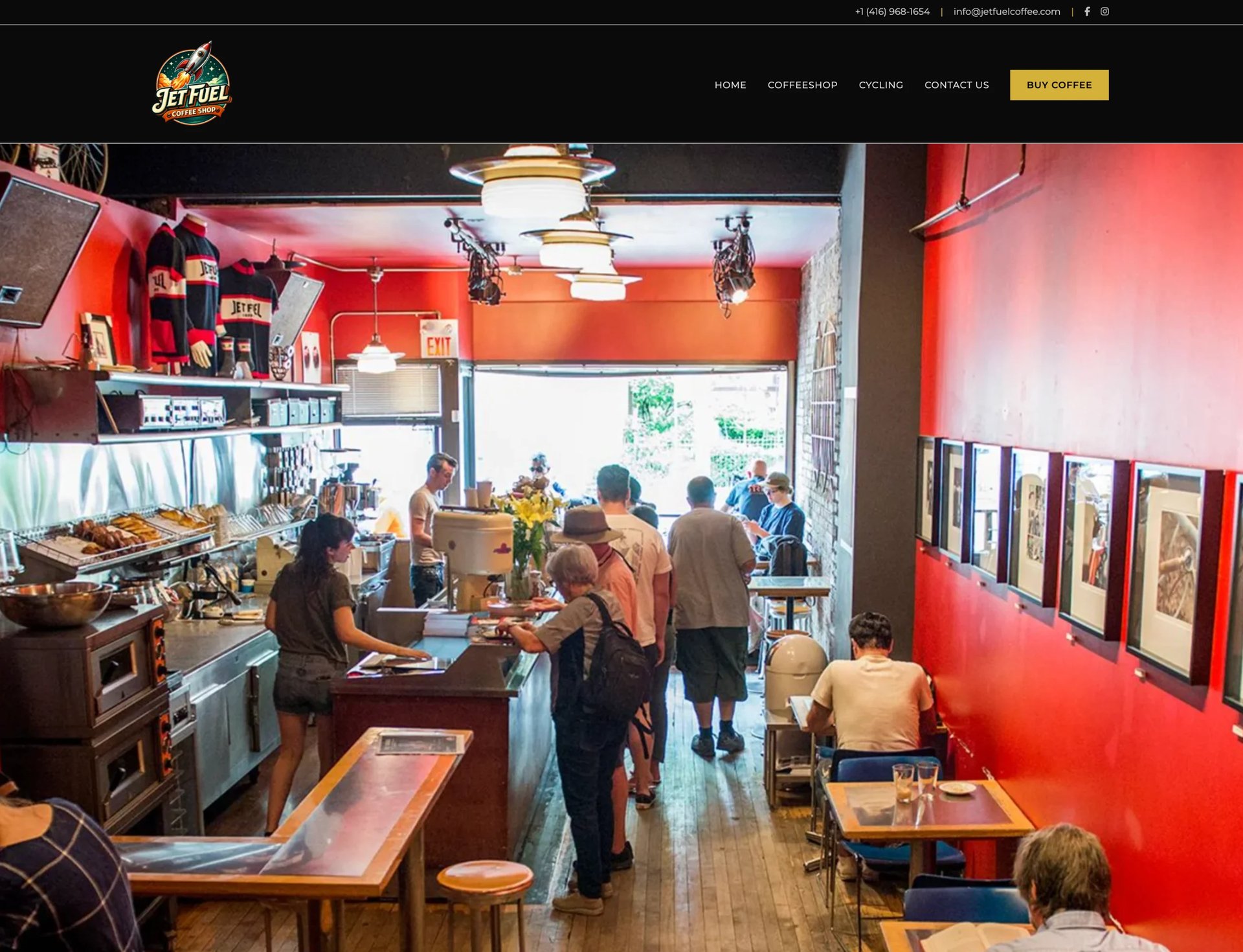 Vibrant red-walled cafe interior with customers at counter, wooden tables, kitchen area, and framed artwork on walls